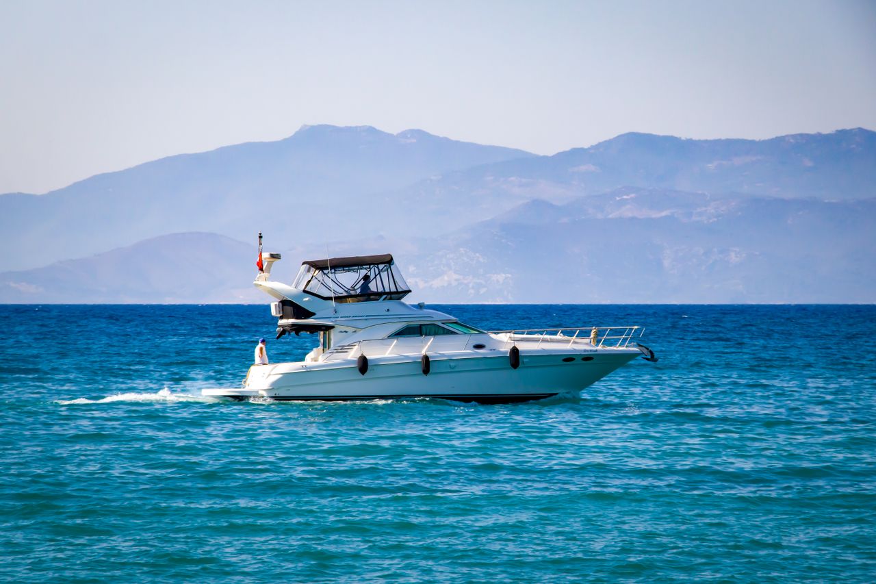 services-01 Elegant yacht sailing on calm blue ocean with a scenic mountain backdrop.